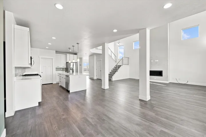 Open-concept living space featuring wood-finish flooring, a modern kitchen with a central island, a built-in fireplace, and a staircase with a cable railing