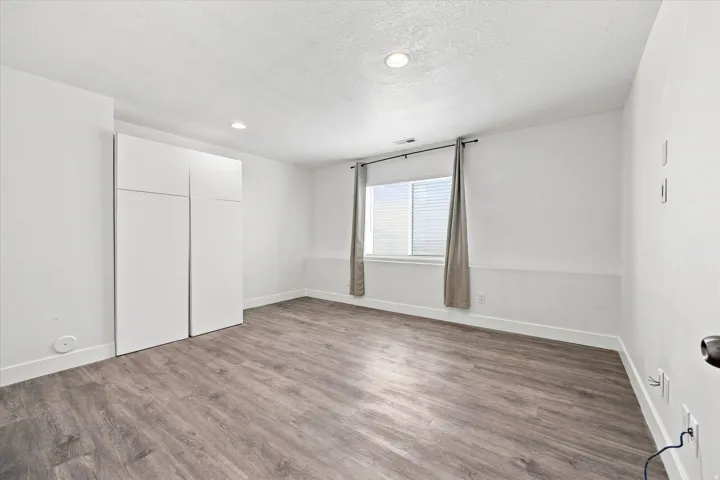 Recessed lighting, wood-finish flooring, white walls, built-in cabinetry, and a window with blinds