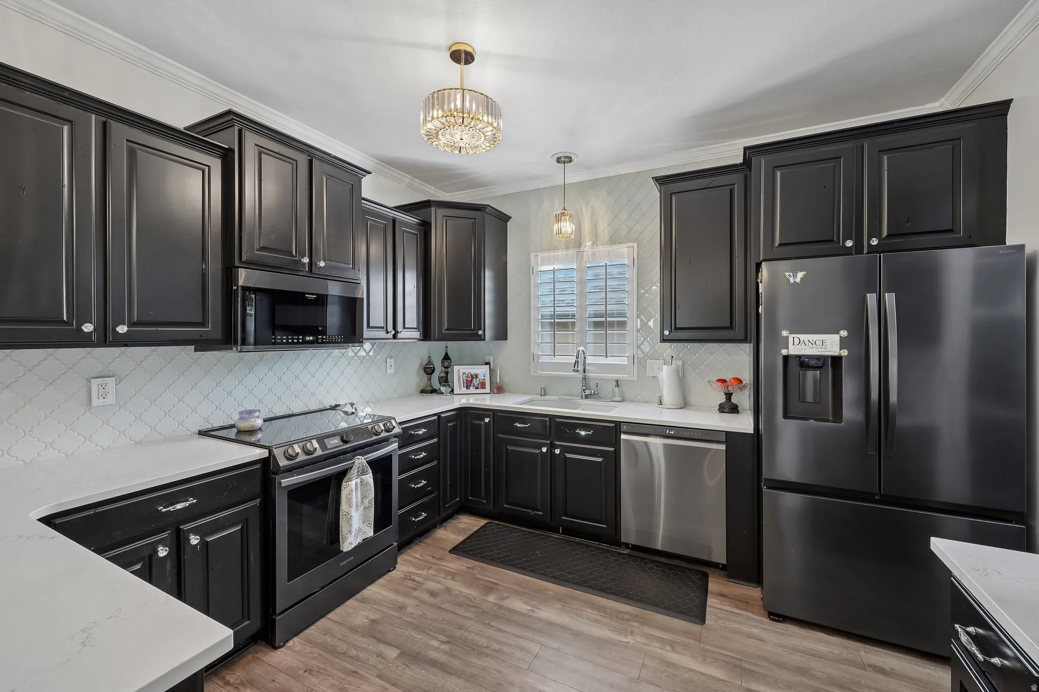 Kitchen featuring dark wood-finish cabinetry, light countertops, wood-finish flooring, a patterned tile backsplash, and stainless steel appliances