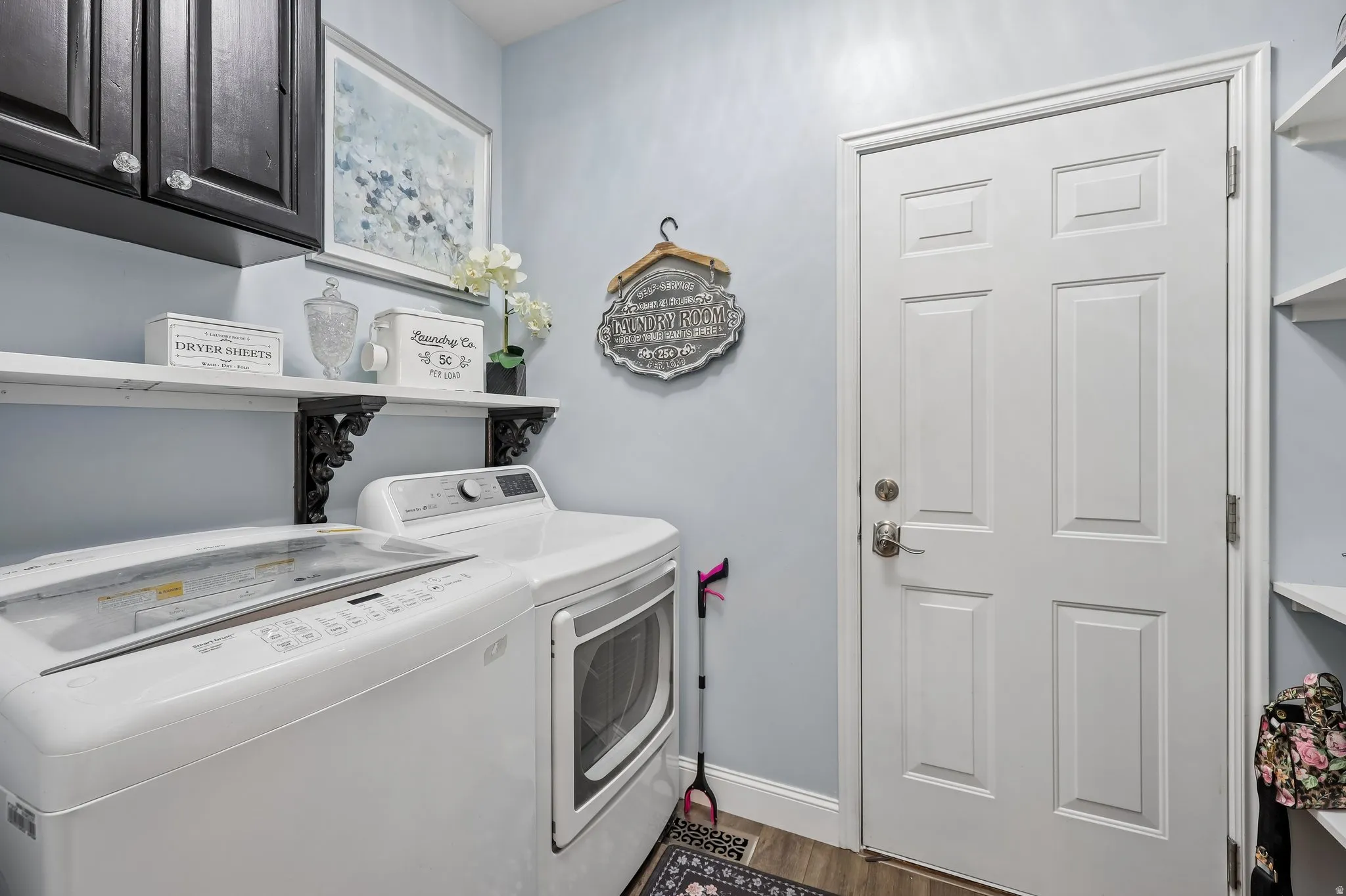 Laundry area featuring wood-finish flooring, wall-mounted shelving, built-in cabinetry, and a paneled door