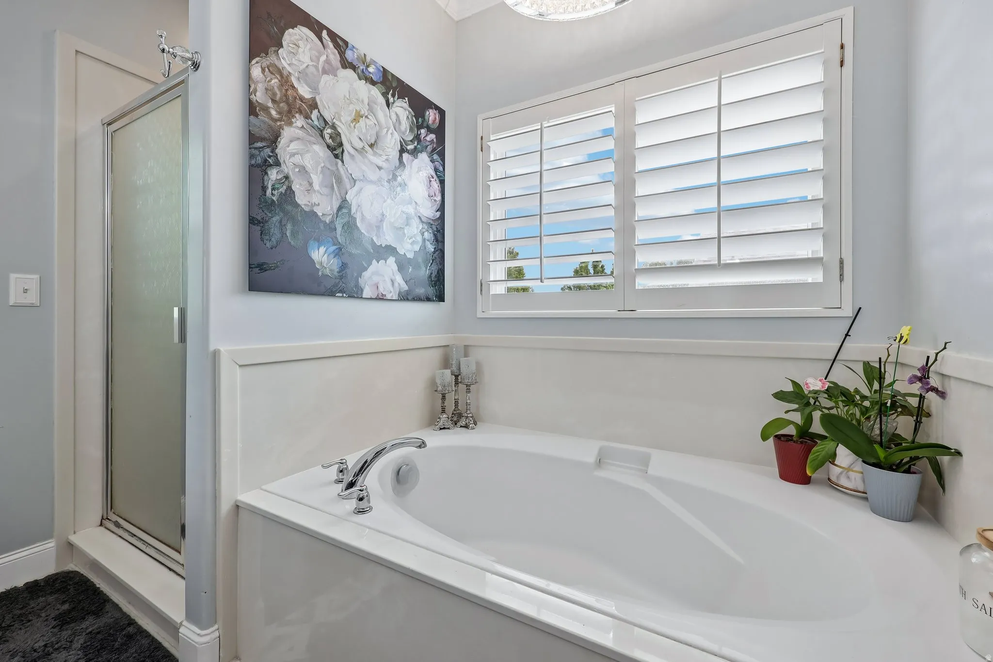 Built-in soaking tub with chrome fixtures, framed window with plantation shutters, and a walk-in shower with a glass door