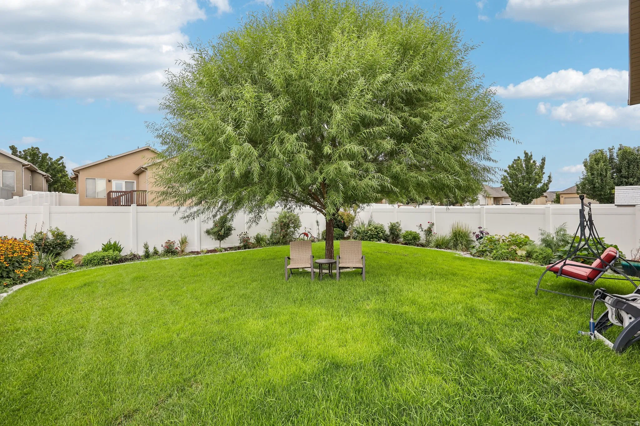 Expansive lawn featuring a mature shade tree, perimeter landscaping, and a white privacy fence