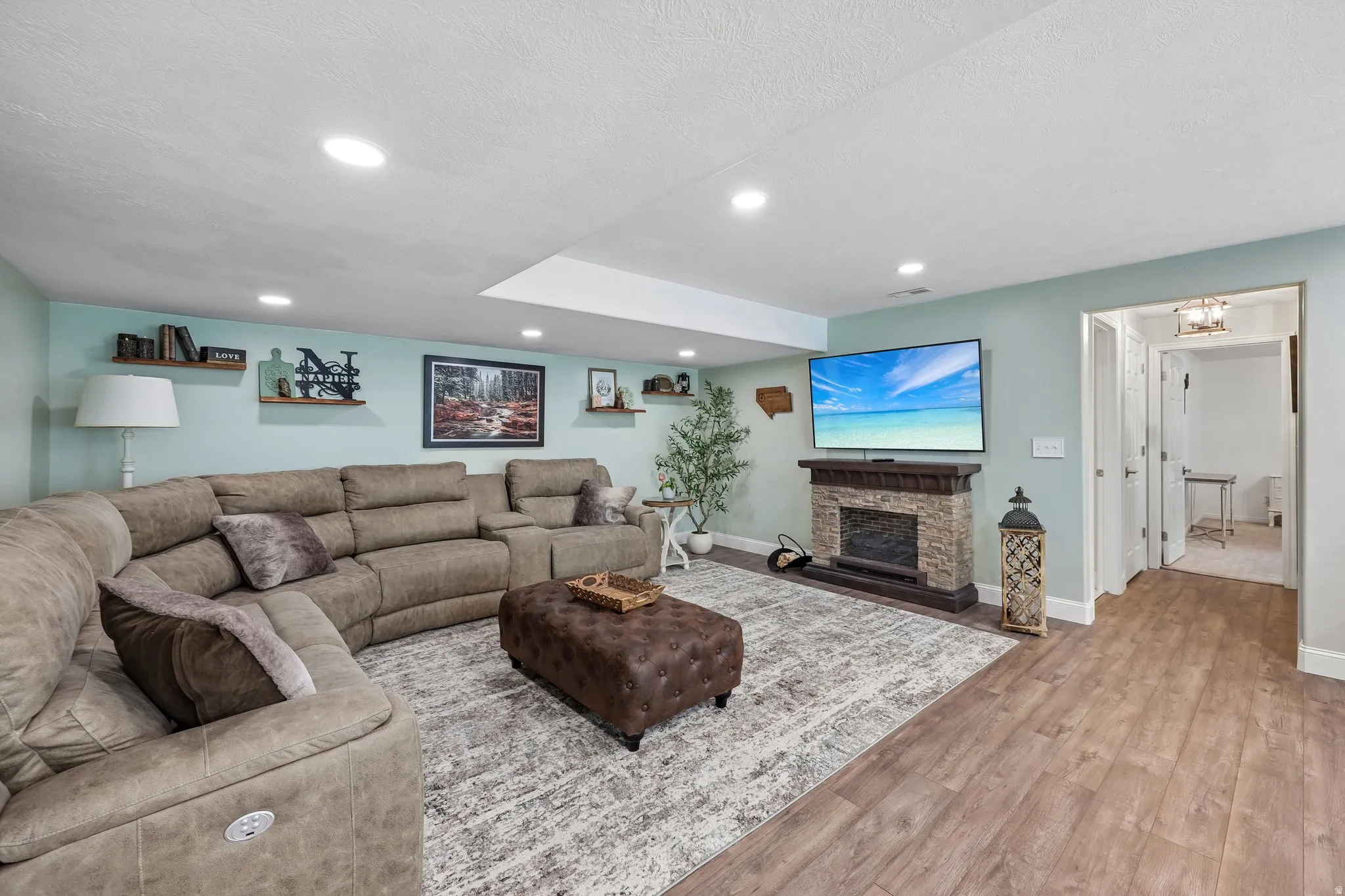 Recessed lighting, wood-finish flooring, stone-clad fireplace with mantel, white trim, and wall shelving