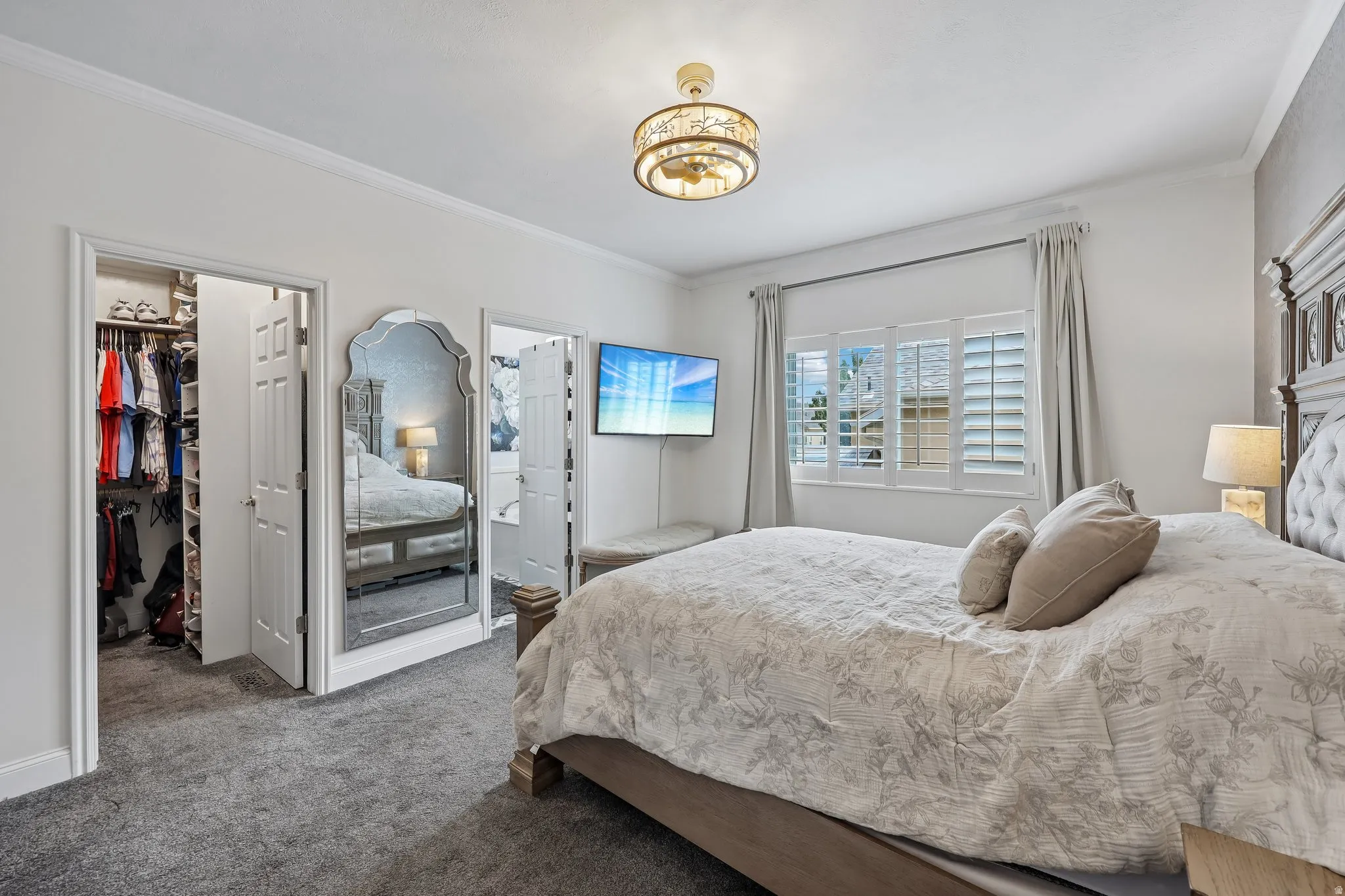 Recessed closet with built-in shelving, decorative wall mirror, window with plantation shutters, crown molding, and flush mount light fixture