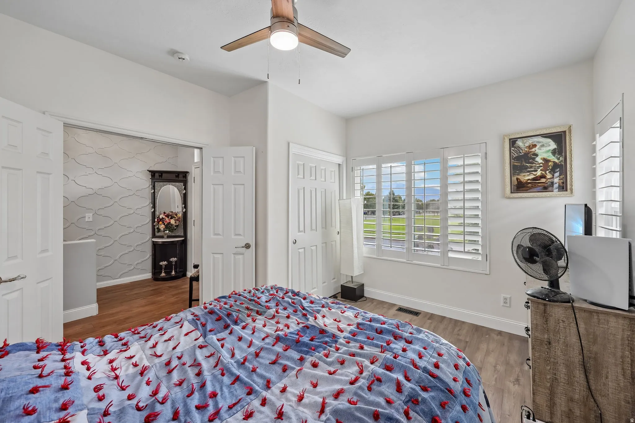 Wood-finish flooring, ceiling fan with integrated lighting, white plantation shutters, and white paneled doors