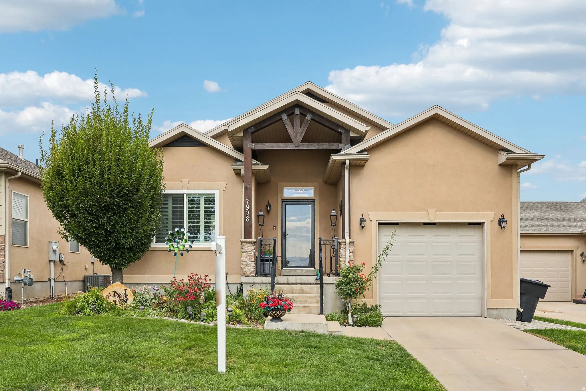Stucco exterior with stone accents, covered entry featuring exposed wood beams, attached garage, and a concrete driveway