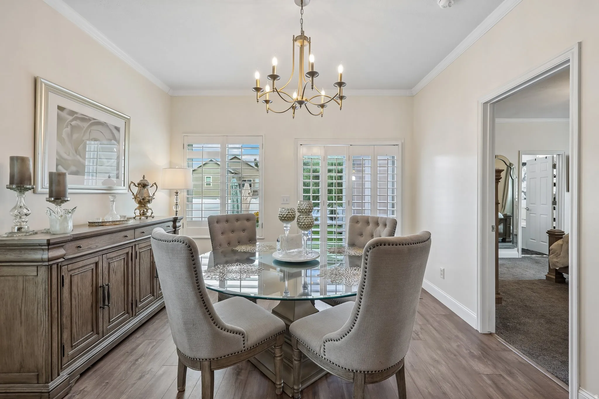 Crown molding, wood-finish flooring, and a multi-arm chandelier illuminate the room