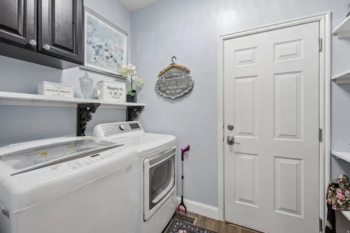 Laundry area featuring wood-finish flooring, wall-mounted shelving, built-in cabinetry, and a paneled door