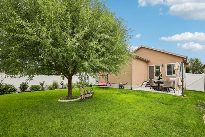 Expansive green lawn, mature tree, concrete patio, and stucco exterior with white fencing