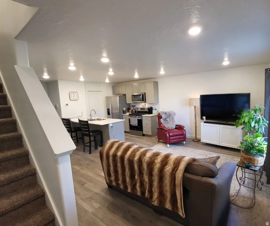 Open-concept living space with recessed lighting, wood-finish flooring, and a kitchen featuring a central island with seating