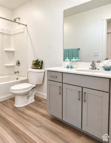 Hall Bathroom White bathtub with shower, wood-finish flooring, white vanity countertop, gray cabinetry, and a large wall-mounted mirror