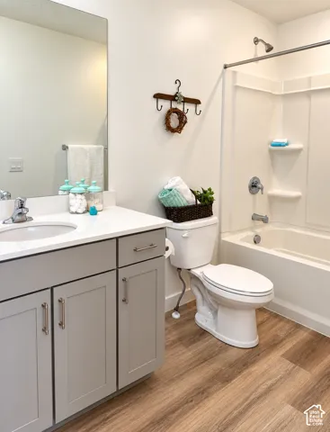 Primary Bathroom featuring a vanity with gray shaker cabinetry, white countertop, integrated sink, a built-in shower/tub combination, and wood-finish flooring