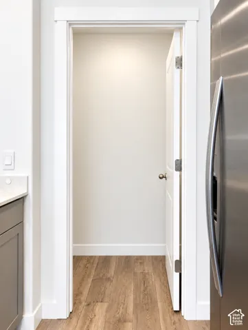 Wood-finish flooring with white baseboards, a white interior door, and brushed nickel hardware