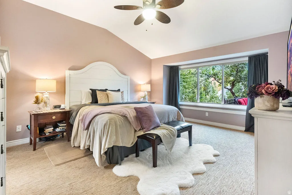 Vaulted ceiling with a ceiling fan, bay window with integrated seating, carpeted flooring, and a white wood-finish headboard