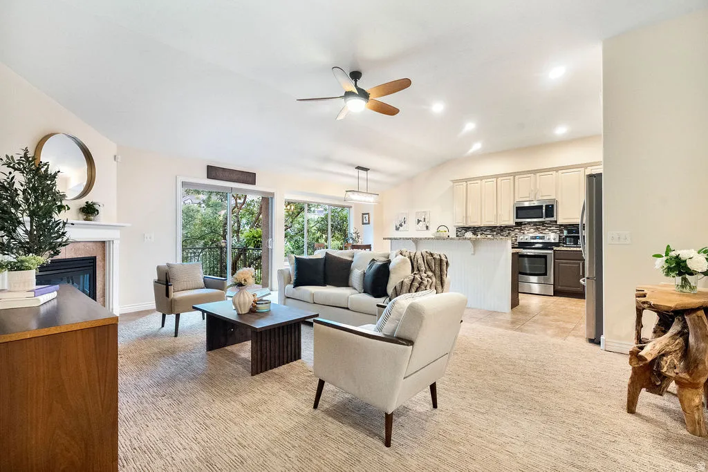 Vaulted ceiling with a ceiling fan, fireplace with a mantel, sliding glass door to exterior, kitchen with stainless steel appliances, and tile flooring