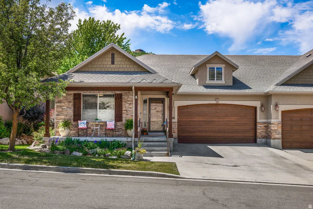 Stone and stucco exterior with a covered porch, wood-finish garage doors, and a dormer window