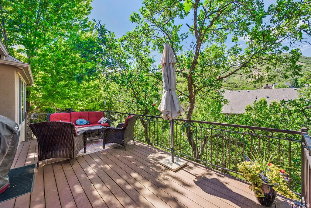 Expansive exterior deck featuring composite decking, decorative metal railing, and mature trees providing natural shading