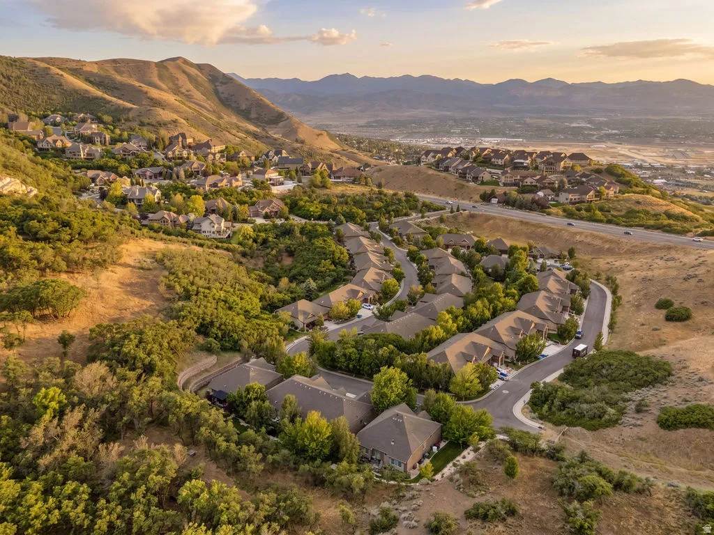 Aerial perspective showcasing a residential community nestled on a hillside with surrounding mountain ranges and a distant urban landscape
