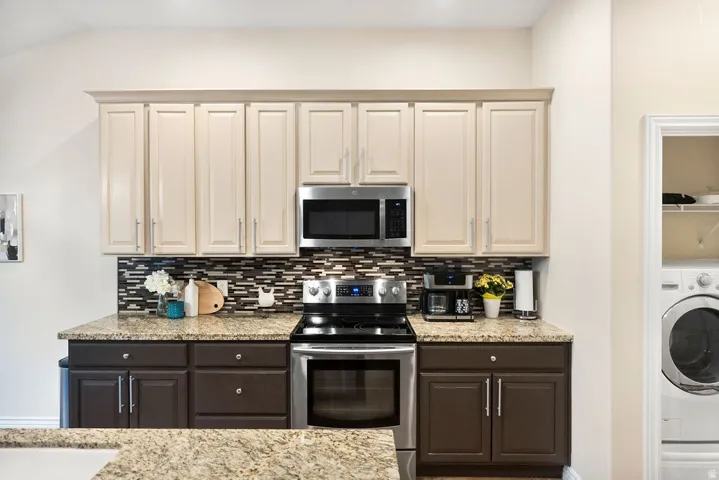 Kitchen featuring two-tone cabinetry, stainless steel appliances, granite-style countertops, and a mosaic tile backsplash