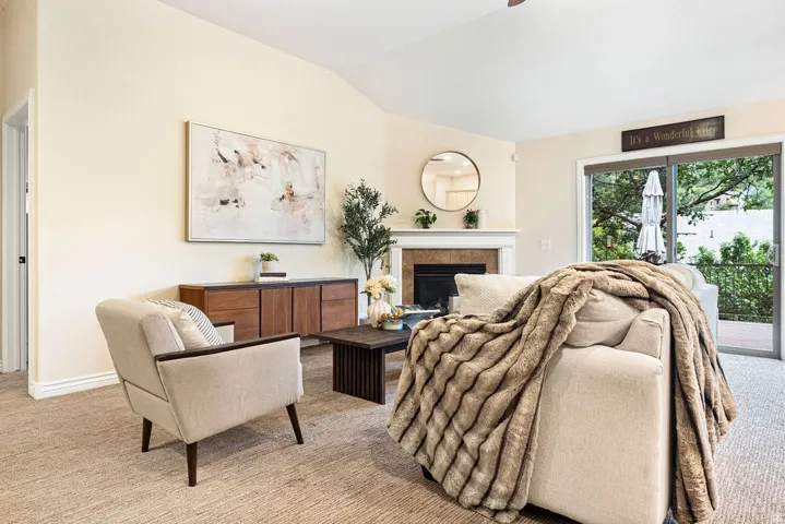 Vaulted ceiling, fireplace with mantel, glass sliding door, and light-toned carpet flooring