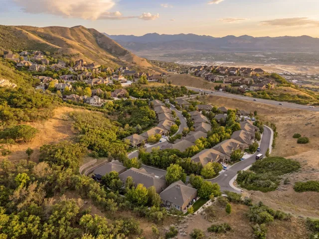 Aerial perspective showcasing a residential community nestled on a hillside with surrounding mountain ranges and a distant urban landscape
