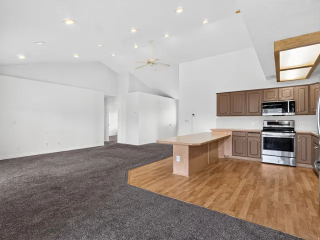 Vaulted ceiling with recessed lighting and ceiling fan, wood-finish flooring, and built-in kitchen cabinetry with stainless steel appliances