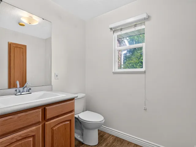 Wood-finish flooring, white vanity with a laminate countertop and integrated sink, chrome faucet fixture, and a toilet