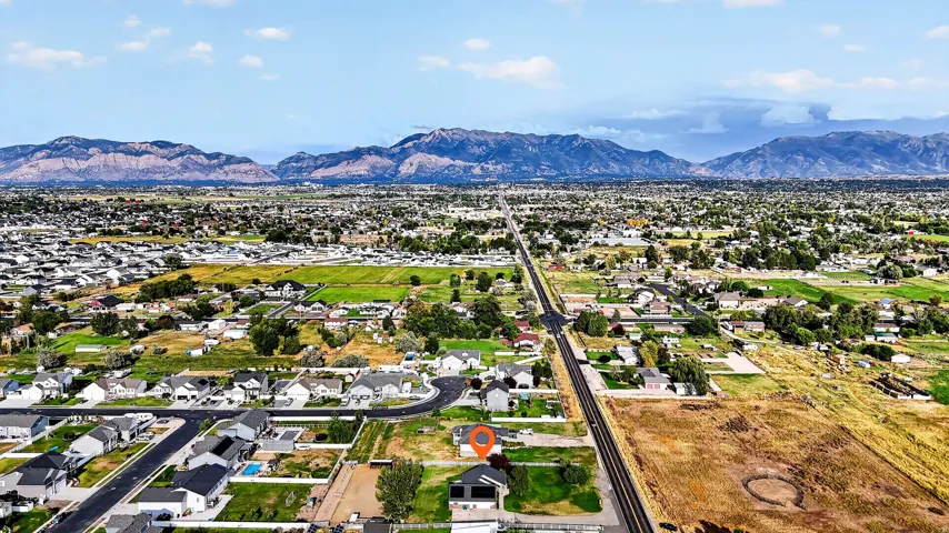 Expansive aerial perspective showcasing a residential development with prominent mountain backdrops, open green spaces, and established infrastructure