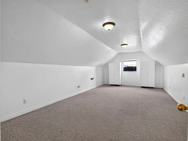 Vaulted ceiling with integrated lighting, window with white trim, and neutral carpet flooring