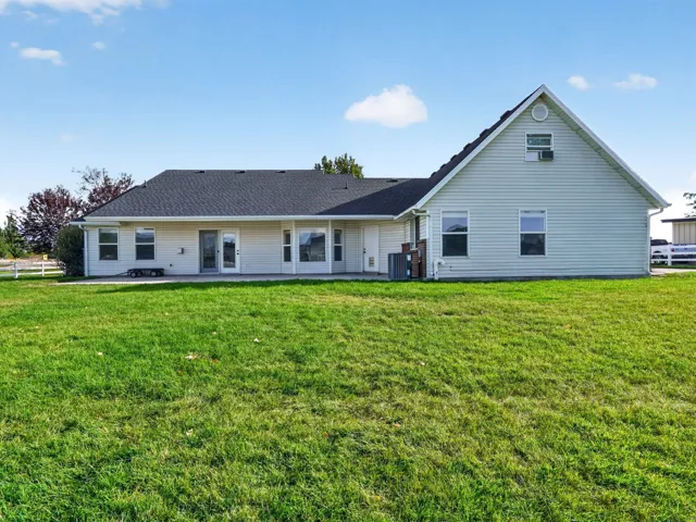 Expansive green lawn surrounding a light-colored, single-story home with multiple windows, a dark shingled roof, and a visible patio area
