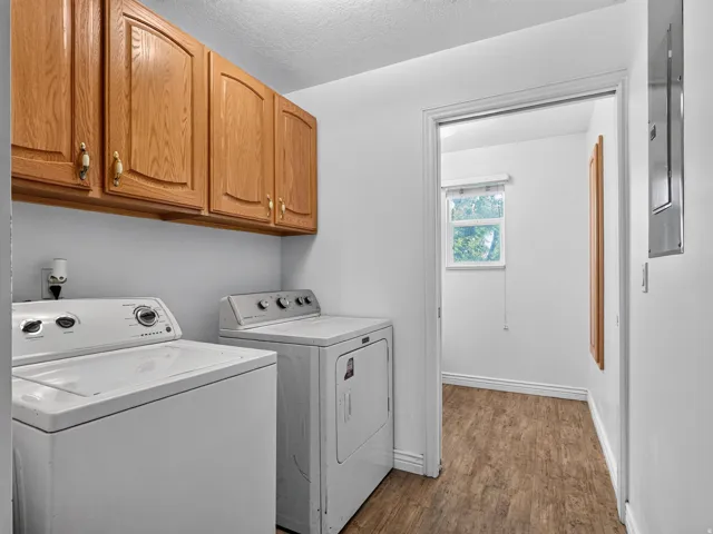 Laundry area featuring wood-finish flooring, overhead cabinetry, and a window in an adjacent room