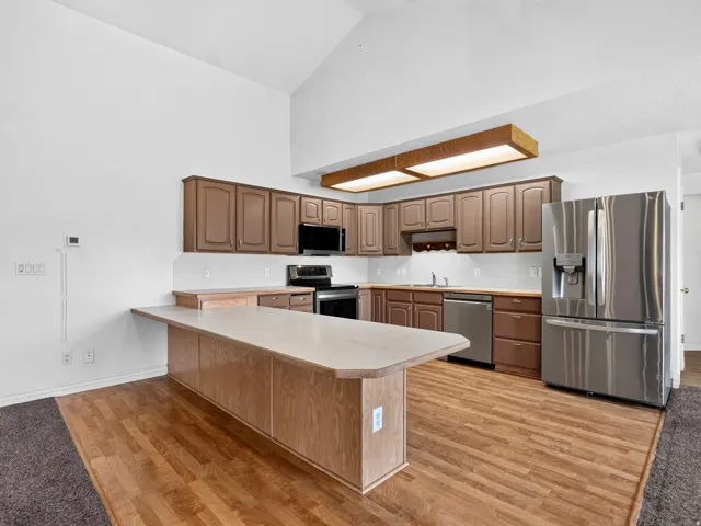 Kitchen featuring wood-finish flooring, vaulted ceiling, built-in cabinetry, stainless steel appliances, and a breakfast bar