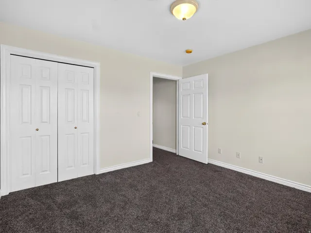 Neutral wall paint, plush carpet flooring, bi-fold closet doors, white trim, and a ceiling-mounted light fixture