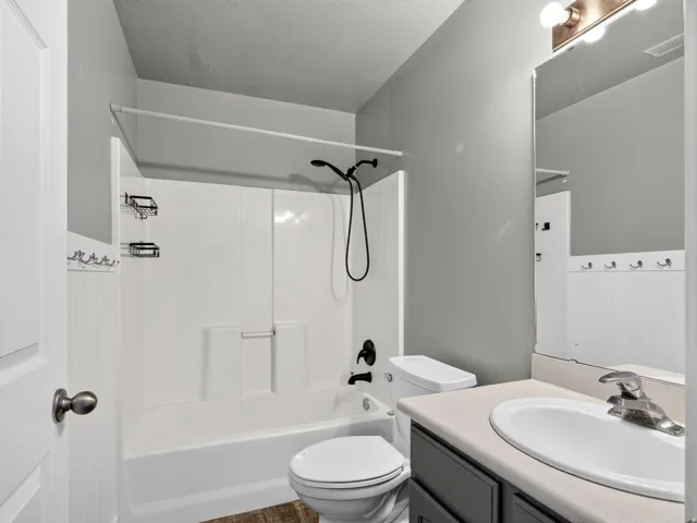 White tub/shower combination with matte black fixtures, white toilet, and wood-finish flooring