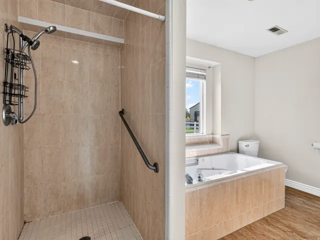 Tiled walk-in shower with a grab bar, large soaking tub, and a window for natural light