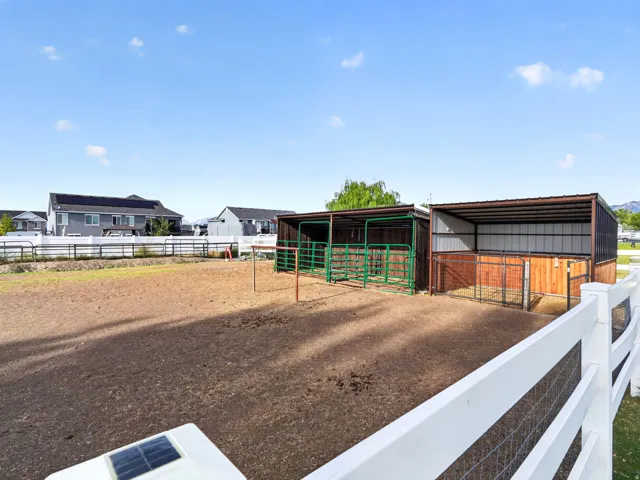 Fenced outdoor area featuring two covered shelters with metal roofing, wood paneling, and green metal gates