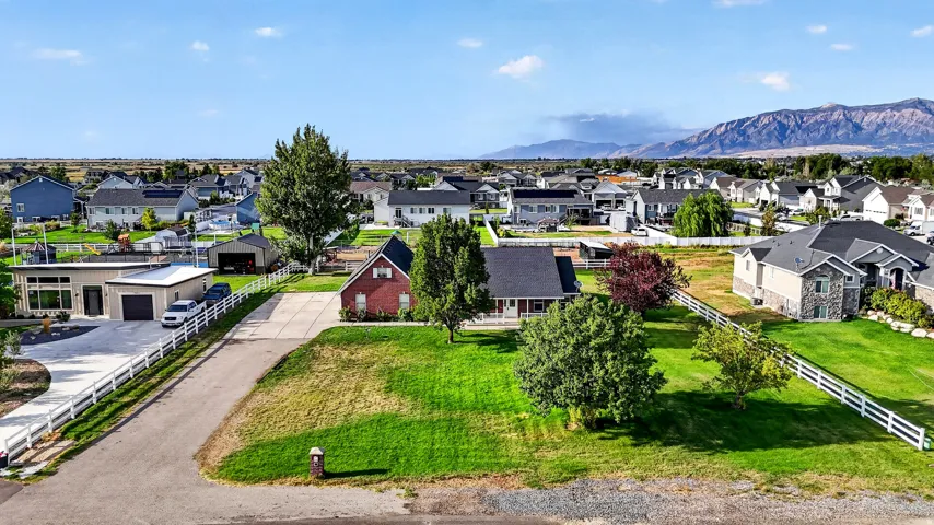 Expansive lot featuring a red brick residence, white fencing, mature trees, and a mountain backdrop