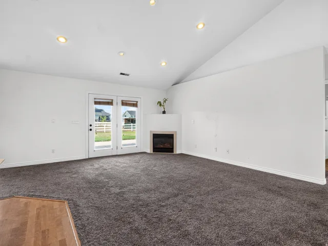 Vaulted ceiling with recessed lighting, double glass-paneled doors, built-in corner fireplace, and dark gray carpeting
