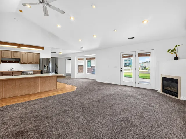 Vaulted ceiling with recessed lighting, kitchen island with wood-finish paneling, built-in stainless steel appliances, double glass-paneled doors, and a gas fireplace with a stone surround