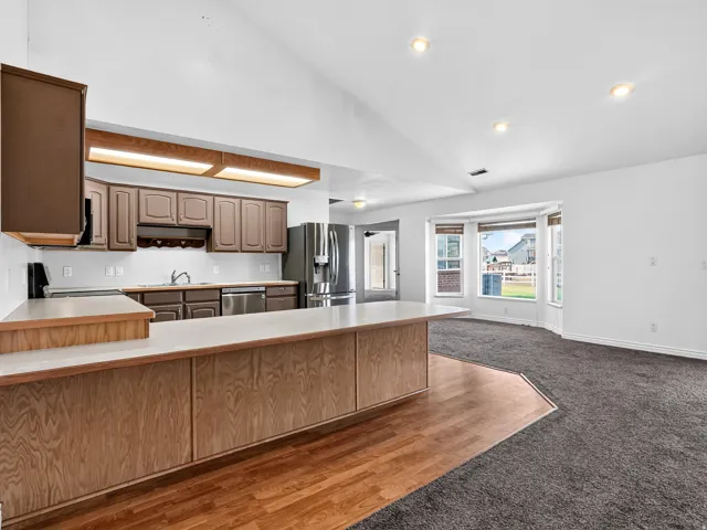 Vaulted ceilings, bay window, wood-finish breakfast bar, dark wood-finish cabinetry, and stainless steel appliances