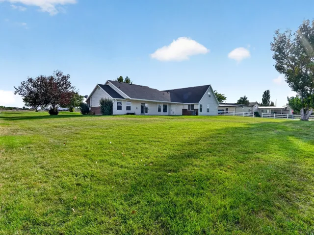 Expansive lawn surrounding the residence, featuring mature trees and a fenced perimeter