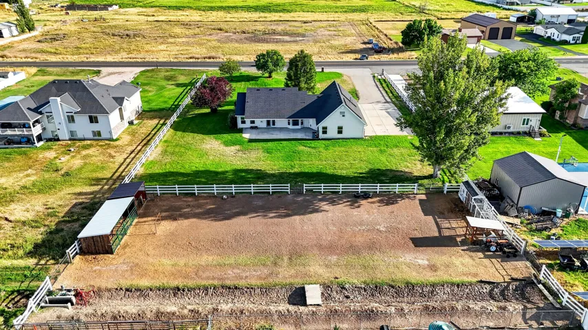 Expansive property featuring a large house with a rear patio, a separate outbuilding, a fenced paddock, and a gravel drive