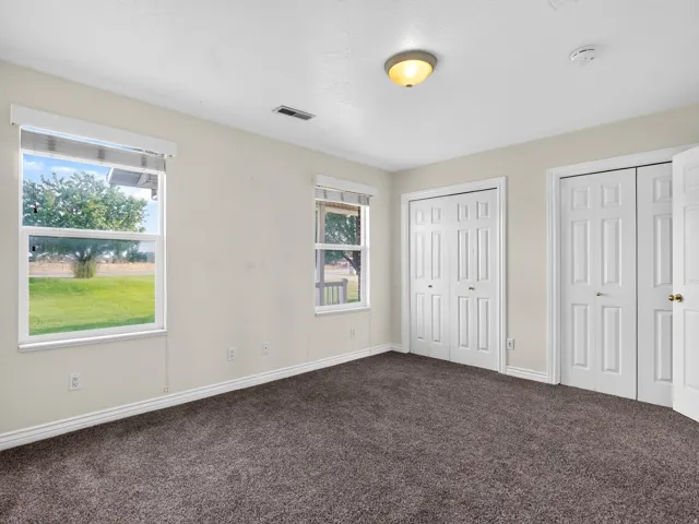 Plush carpet flooring, multiple windows, two paneled closet doors, and a semi-flush mount ceiling light