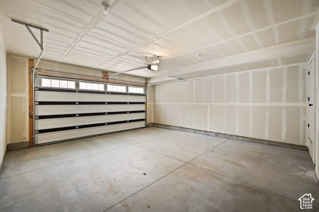 Spacious garage with a concrete floor, overhead lighting, and a white paneled garage door featuring transom windows