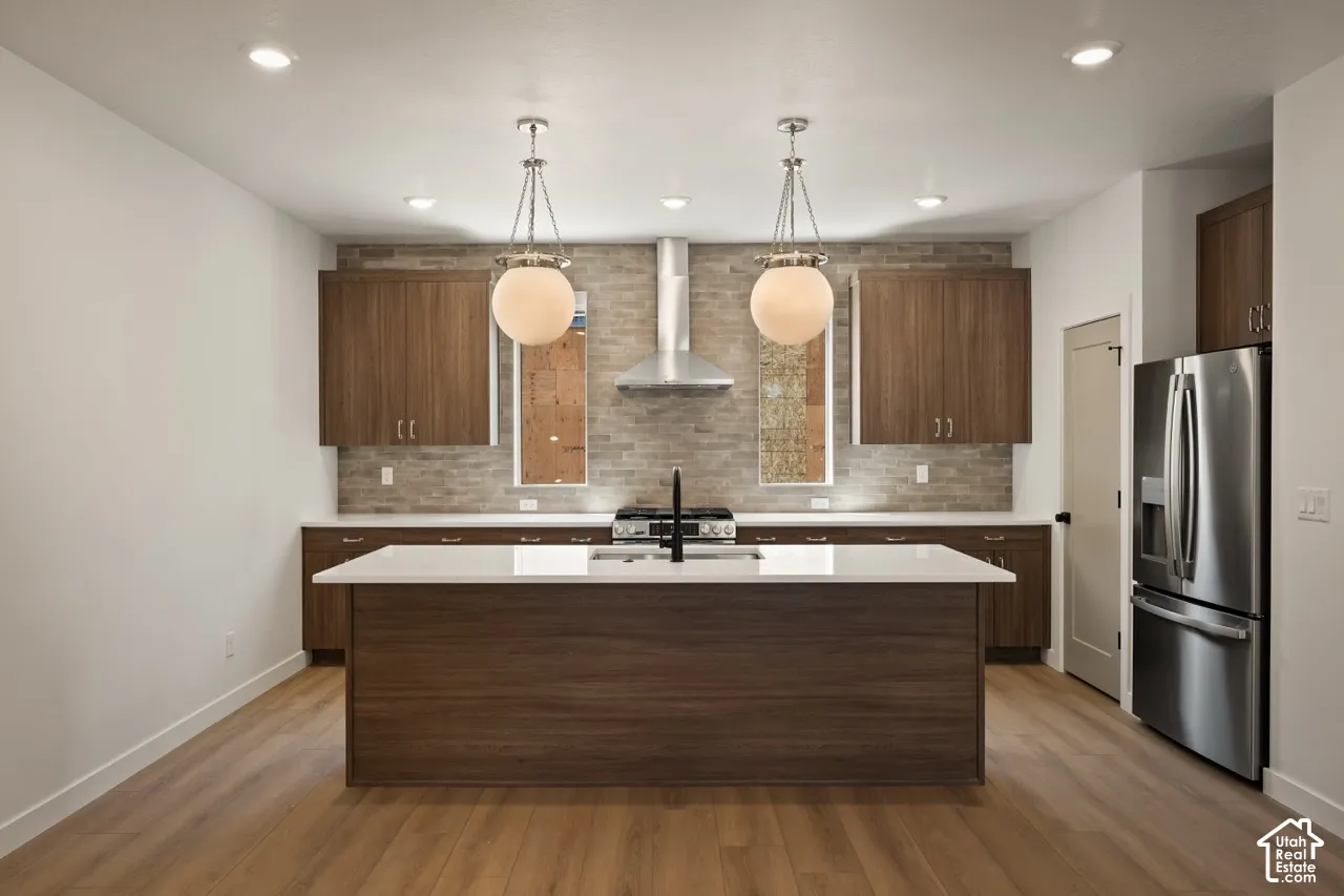 Kitchen featuring a central island with white countertop, wood-finish cabinetry, stainless steel appliances, brick-patterned backsplash, and pendant lighting