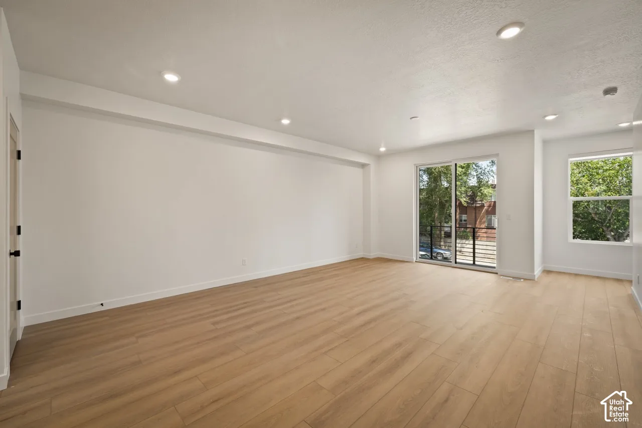 Recessed ceiling lighting, wood-finish flooring, sliding glass door, white trim, and a black door handle