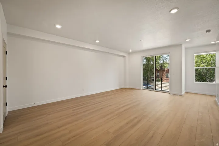 Recessed ceiling lighting, wood-finish flooring, sliding glass door, white trim, and a black door handle