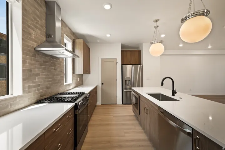 Modern kitchen featuring an expansive island with a matte black faucet, stainless steel appliances, wood-finish cabinetry, and a brick-patterned backsplash