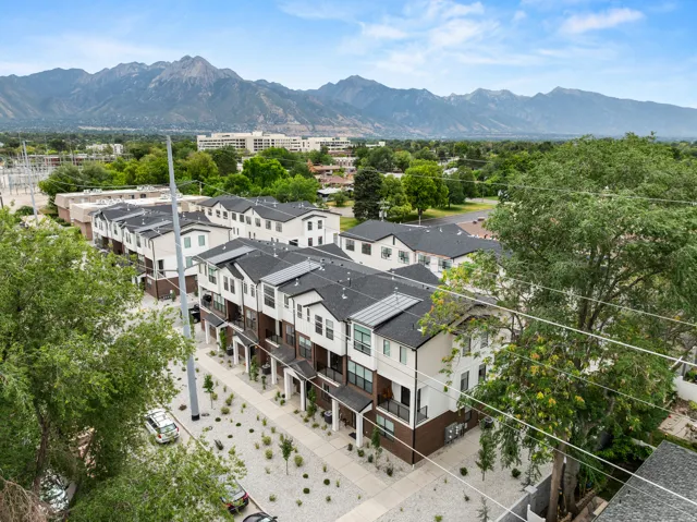 Modern townhome exteriors with dark roofing and light facades, mountain scenery, established trees, and structured landscaping featuring white rock