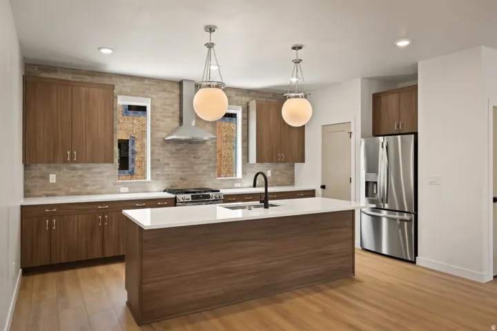 Kitchen featuring wood-finish cabinetry, stainless steel appliances, brick-style backsplash, and a center island with a black faucet